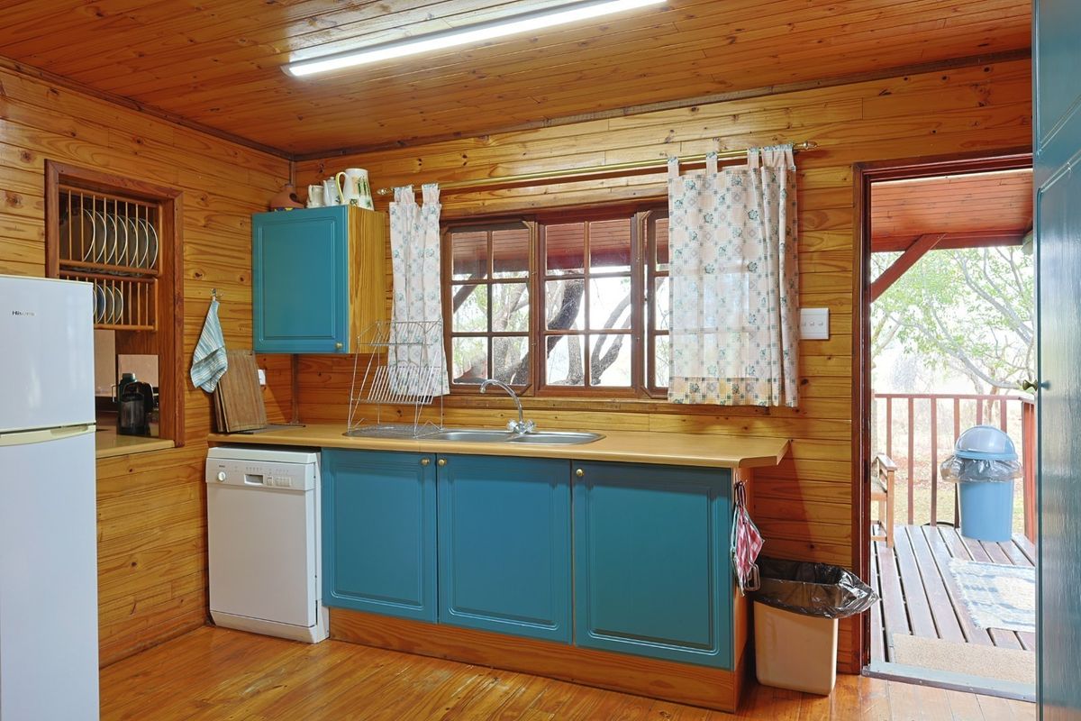 A rustic kitchen featuring timber wall paneling, wooden cabinetry, a stainless steel sink, and direct access to an outdoor deck area.