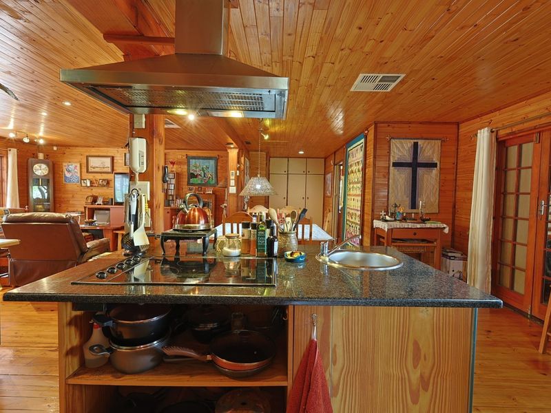 Open-plan kitchen featuring a central island with granite countertops, electric cooktop, and stainless steel extractor fan, set within a warm timber-paneled interior.