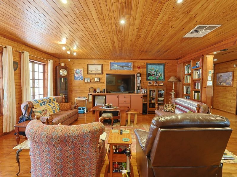 A cozy living room featuring extensive timber wall and ceiling cladding, polished timber flooring, and built-in shelving units.