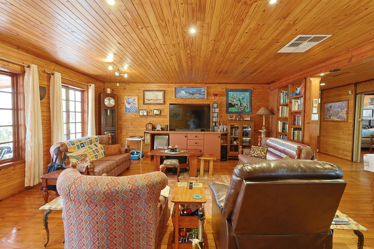 A cozy living room featuring extensive timber wall and ceiling cladding, polished timber flooring, and built-in shelving units.