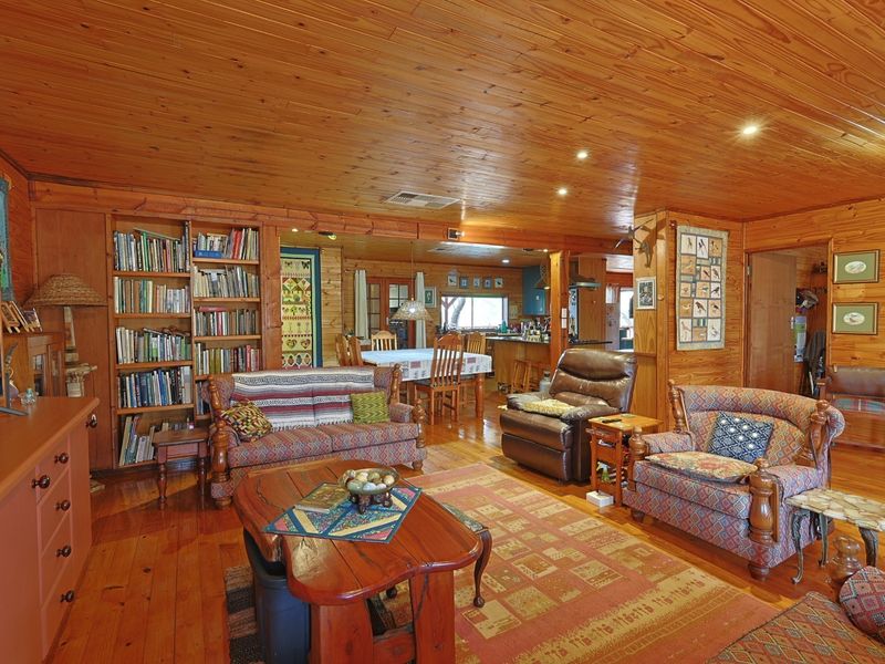 Spacious open-plan living and dining area featuring warm timber wall cladding, ceiling, and flooring, with a built-in bookshelf and integrated kitchen space.