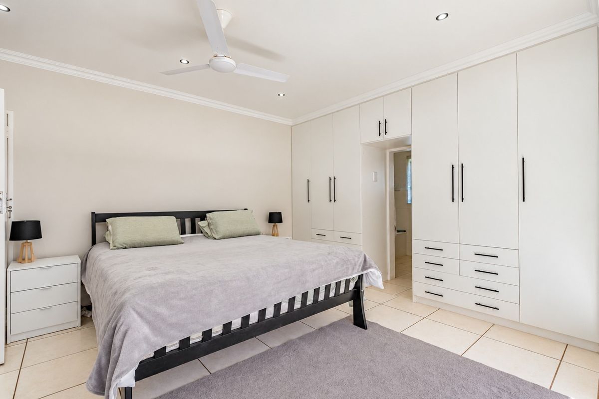 Spacious bedroom featuring extensive built-in cabinetry, tiled flooring, a ceiling fan, and recessed lighting, with an integrated doorway leading to an en-suite bathroom.