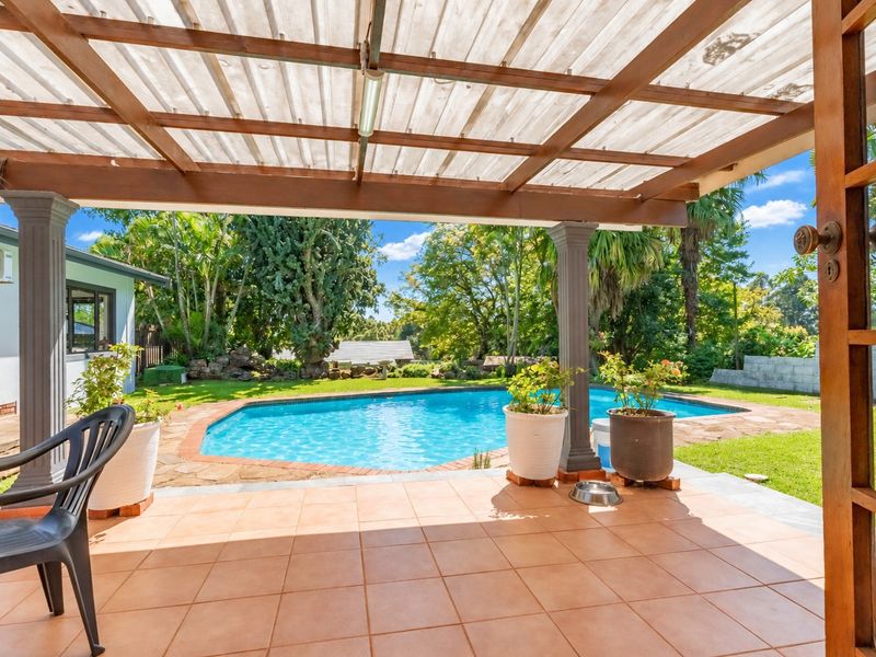 Covered patio area featuring a timber pergola and tiled flooring, overlooking a private swimming pool and landscaped garden.