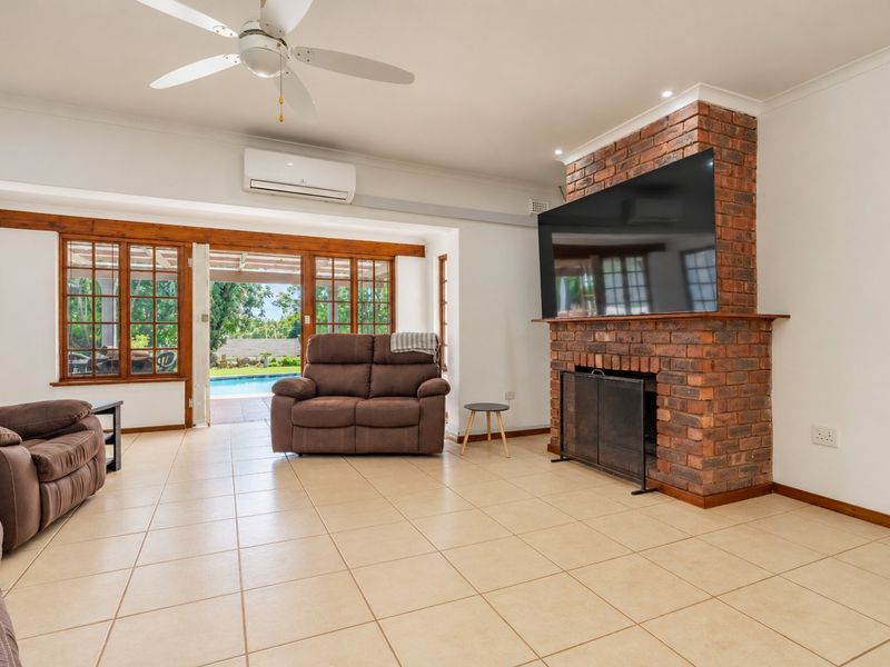 Spacious living room featuring an exposed brick fireplace, tiled flooring, and large timber-framed sliding doors providing seamless access to the outdoor pool area.