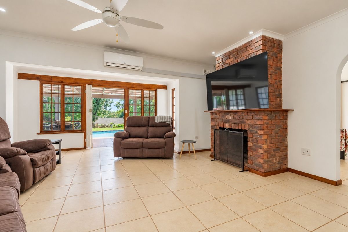 Spacious living room featuring an exposed brick fireplace, tiled flooring, and large timber-framed sliding doors providing seamless access to the outdoor pool area.