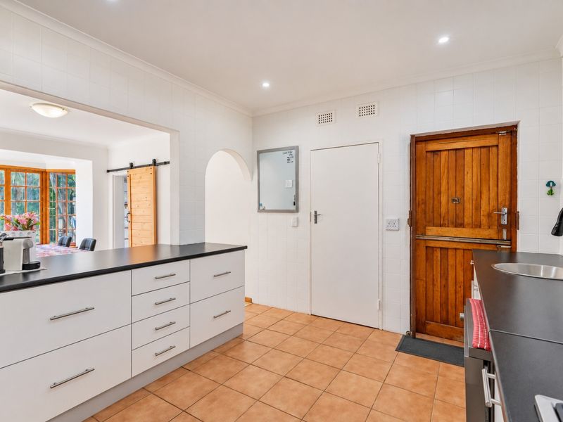A functional kitchen featuring white cabinetry, dark countertops, tiled flooring, and a distinctive wooden stable door leading to the exterior.