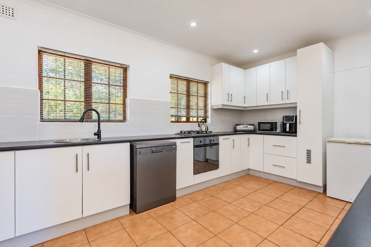 A clean, functional kitchen featuring white cabinetry, dark countertops, built-in oven, gas cooktop, and tiled flooring with ample natural light.