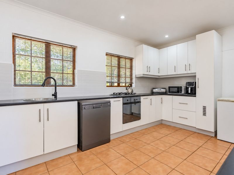 A clean, functional kitchen featuring white cabinetry, dark countertops, built-in oven, gas cooktop, and tiled flooring with ample natural light.