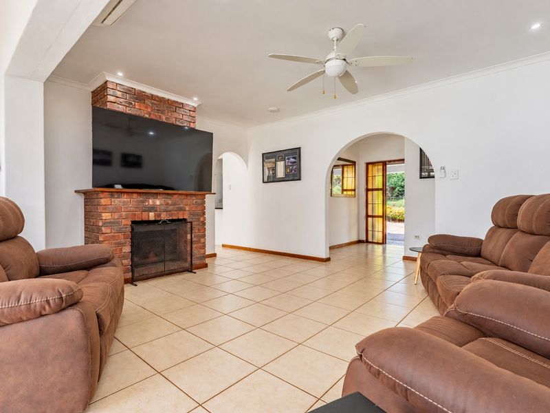 Spacious living room featuring a classic brick fireplace, tiled flooring, and an arched entryway leading to the exterior.