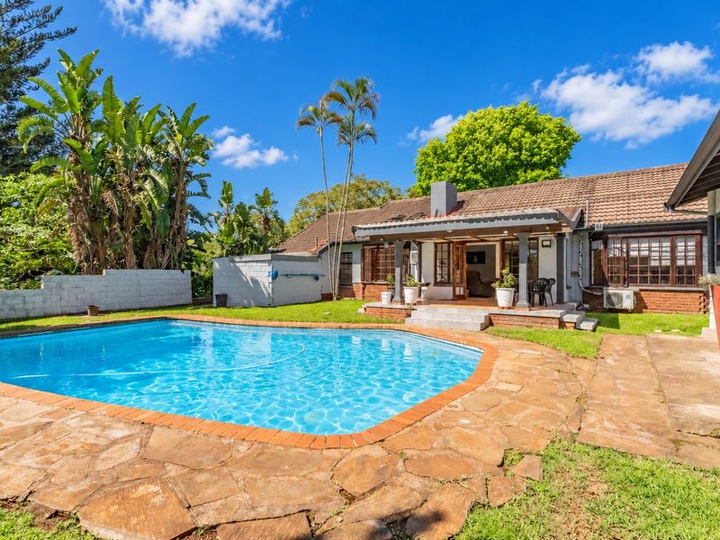 A spacious backyard featuring a swimming pool, stone-paved patio, and a covered veranda, perfect for outdoor entertaining and relaxation.