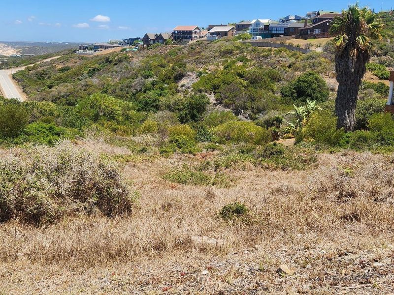 A view of the vacant residential land featuring sloped terrain with coastal and neighbourhood surroundings in the distance.
