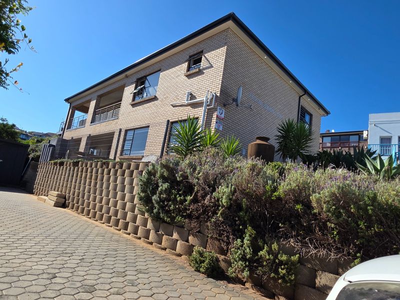 A multi-story brick residential building featuring a paved driveway, retaining wall, and an upper-level balcony.