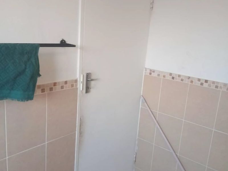 A functional bathroom space featuring neutral wall and floor tiling, a standard door, and a wall-mounted towel rail.