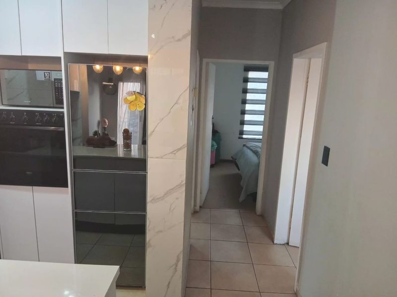 Modern kitchen area featuring built-in oven and microwave, marble-look pillar detail, and tiled flooring, leading into a hallway and bedroom.