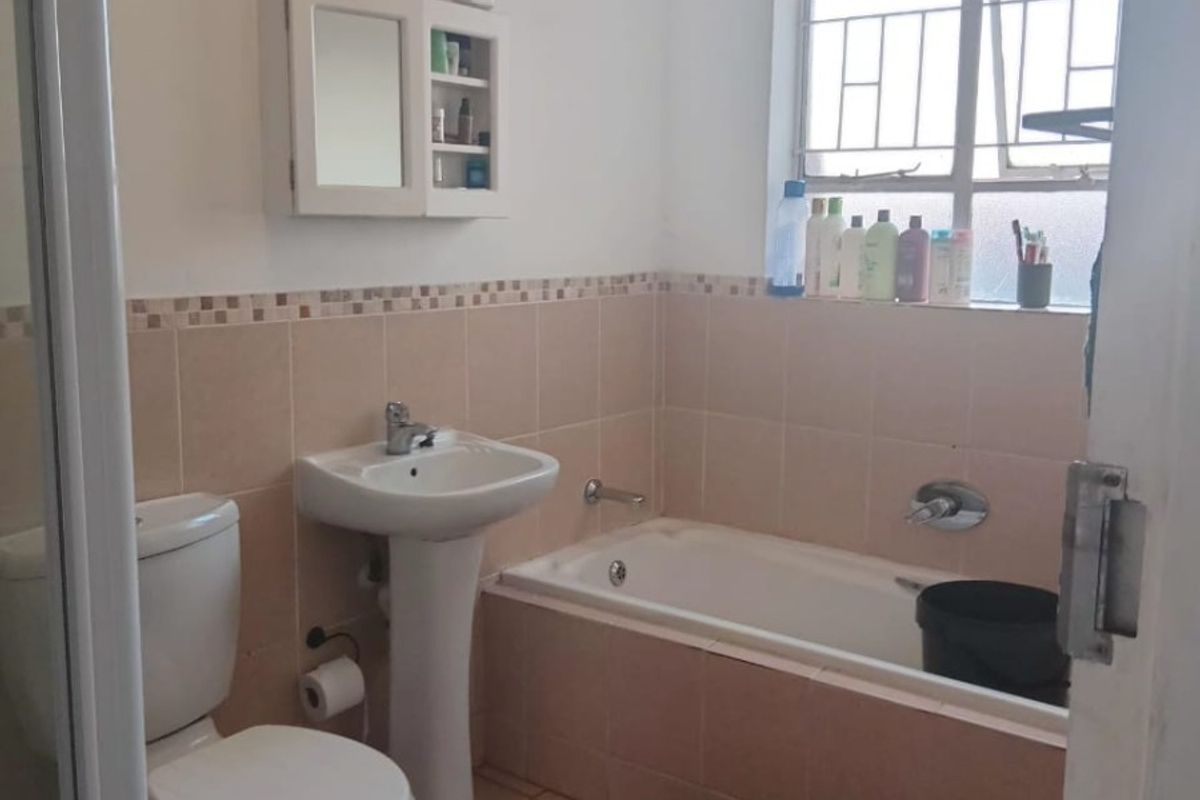 A functional bathroom featuring a pedestal basin, toilet, and bathtub with neutral wall tiling and a window with security bars.