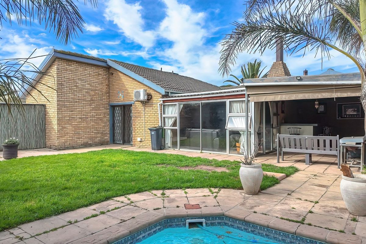 Rear exterior view featuring a swimming pool, lawn, brick facade, and a covered patio area with an outdoor fireplace.