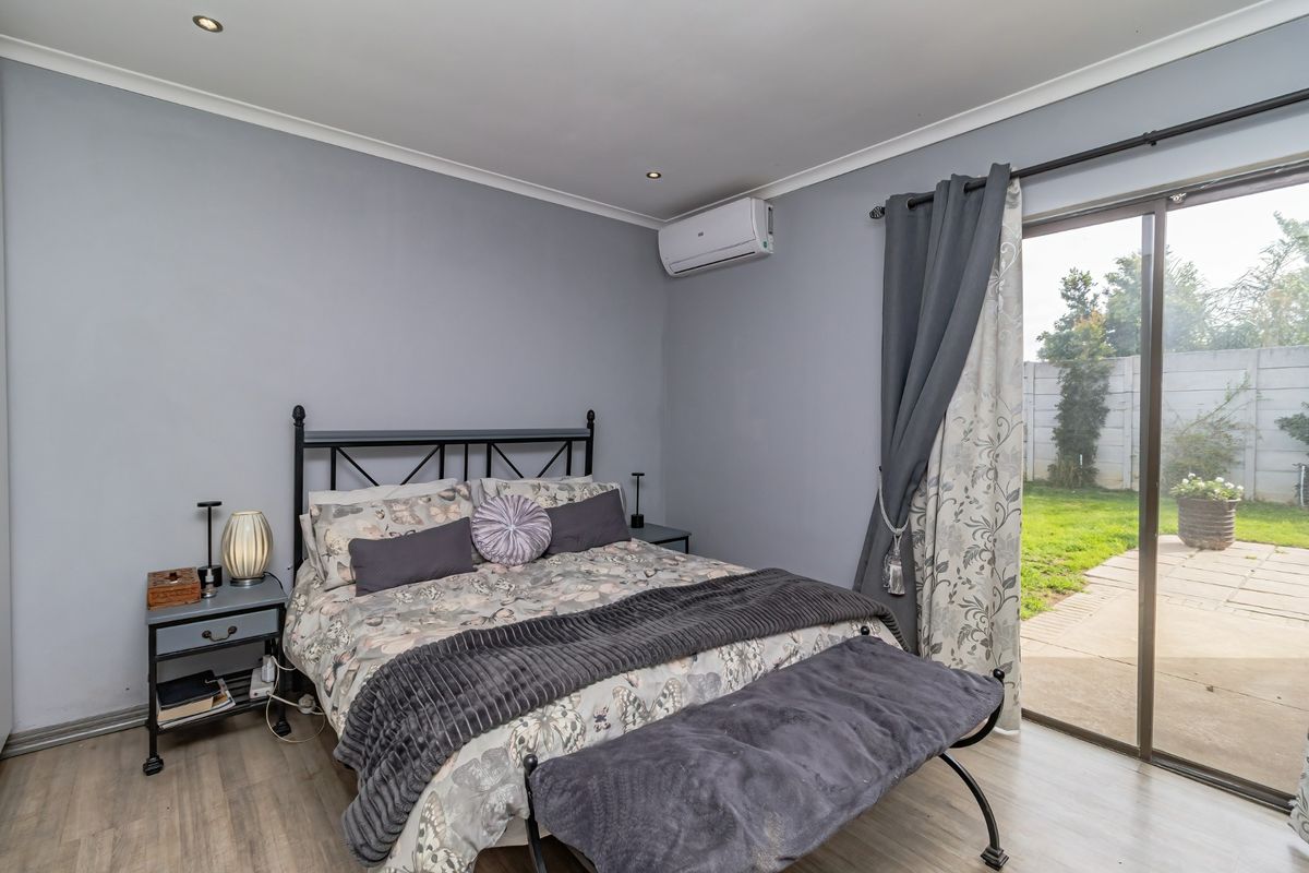 A well-maintained bedroom featuring laminate flooring, recessed lighting, a wall-mounted air conditioner, and direct access to the rear garden via a sliding glass door.