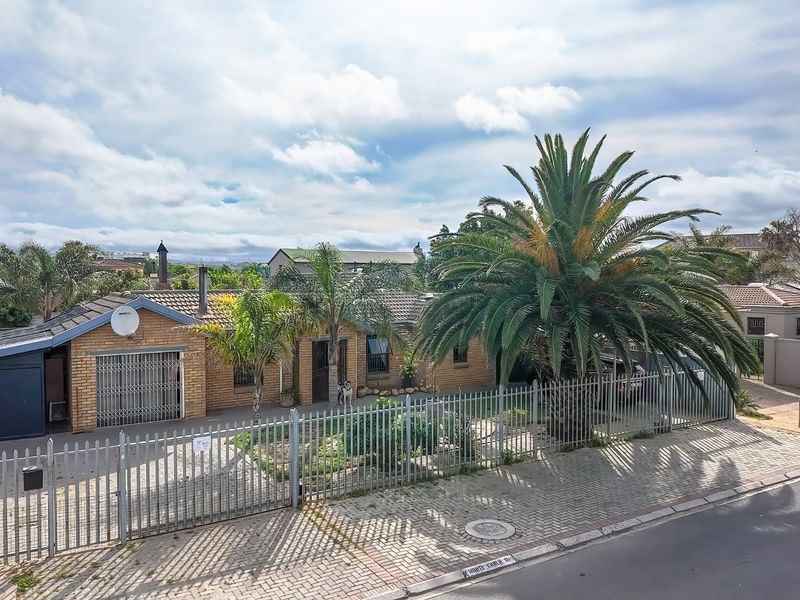 Front view of a single-story face brick house featuring a tiled roof, paved driveway, and secure perimeter fencing with a large palm tree.