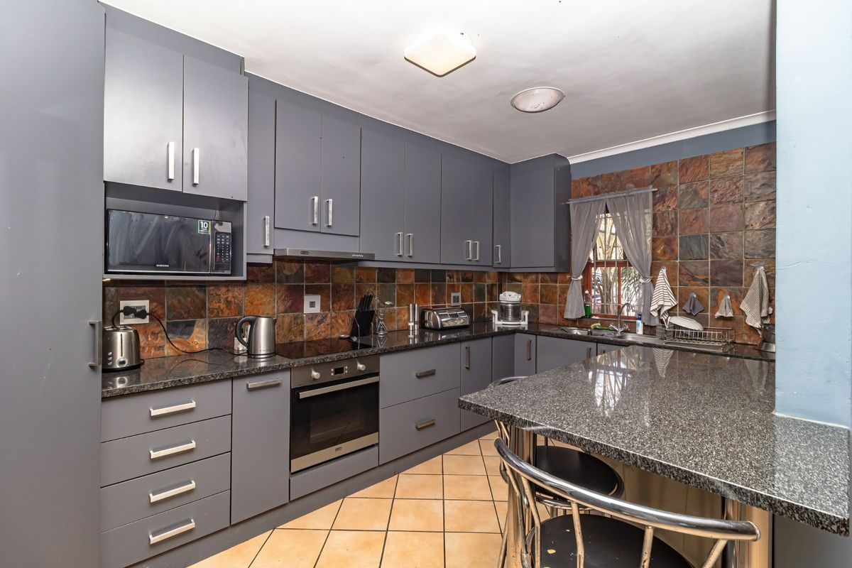 A functional kitchen featuring grey built-in cabinetry, granite countertops, integrated appliances, and a tiled backsplash with a breakfast nook.