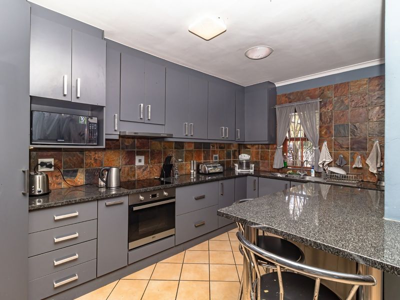 A functional kitchen featuring grey built-in cabinetry, granite countertops, integrated appliances, and a tiled backsplash with a breakfast nook.
