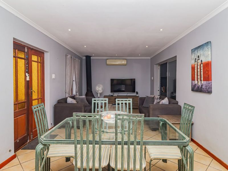 Open-plan living and dining area featuring tiled flooring, a wood-burning fireplace, and a wall-mounted air conditioning unit.