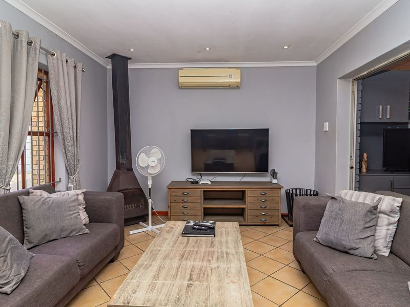 A comfortable living room featuring a freestanding fireplace, split-system air conditioning, and tiled flooring, with direct access to an adjacent space via sliding doors.