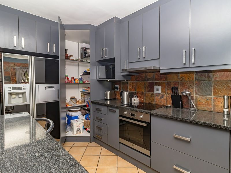 Modern kitchen featuring dark grey cabinetry, granite countertops, built-in oven, electric hob, extractor fan, and a convenient integrated pantry cupboard.