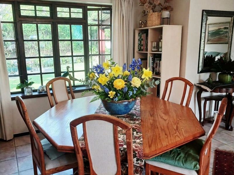 A dining area featuring tiled flooring and a large multi-pane timber window overlooking the garden.