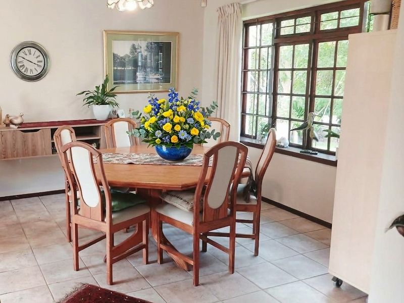 A dining room featuring tiled flooring, coved ceilings, and large timber-framed windows that provide natural light and garden views.