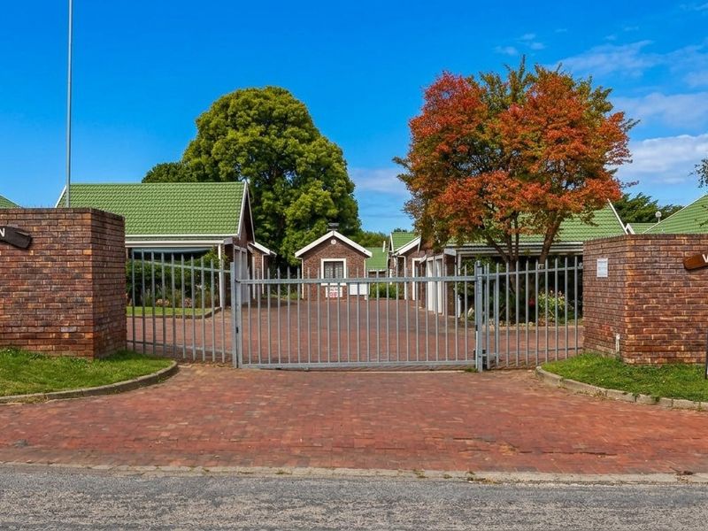Front entrance view of Heron Village townhouse complex featuring a brick perimeter wall, metal security gate, and paved driveway access.