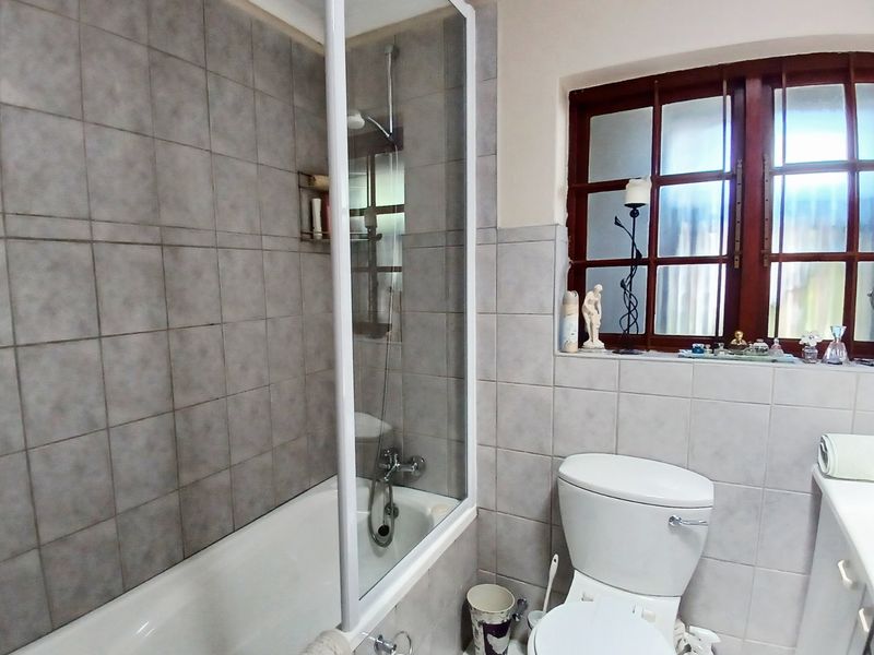 A functional bathroom featuring a bathtub with a glass shower screen, a standard toilet, and tiled wall finishes with a timber-framed window.