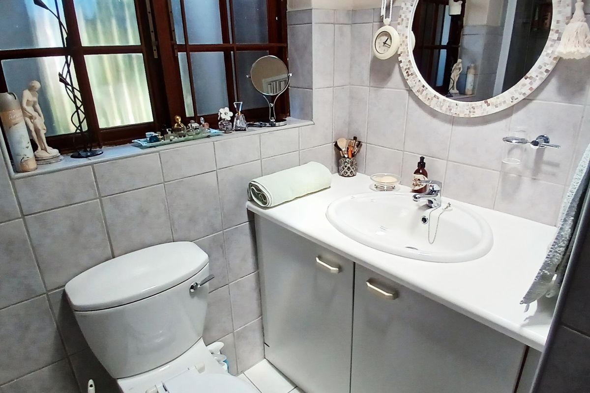 A compact bathroom featuring a vanity cabinet with an integrated basin, a standard toilet, and tiled finishes throughout, complemented by a timber-framed window.