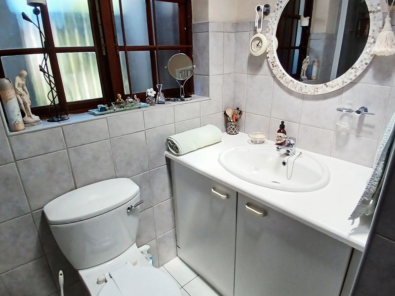 A compact bathroom featuring a vanity cabinet with an integrated basin, a standard toilet, and tiled finishes throughout, complemented by a timber-framed window.