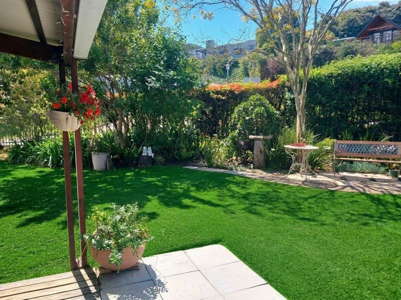 A well-maintained covered patio area overlooking a lush, landscaped garden with artificial turf and mature trees.