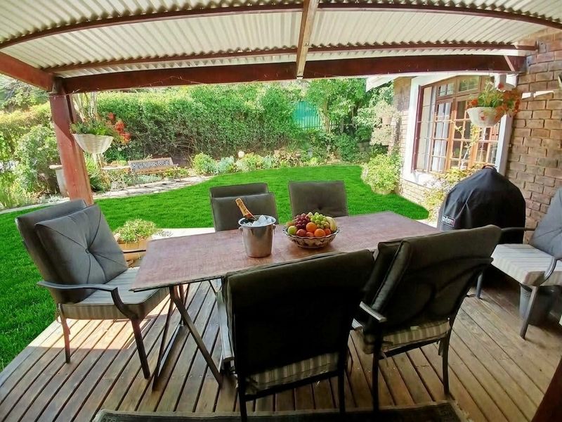 A covered outdoor patio featuring timber decking and exposed brickwork, overlooking a well-maintained garden area.