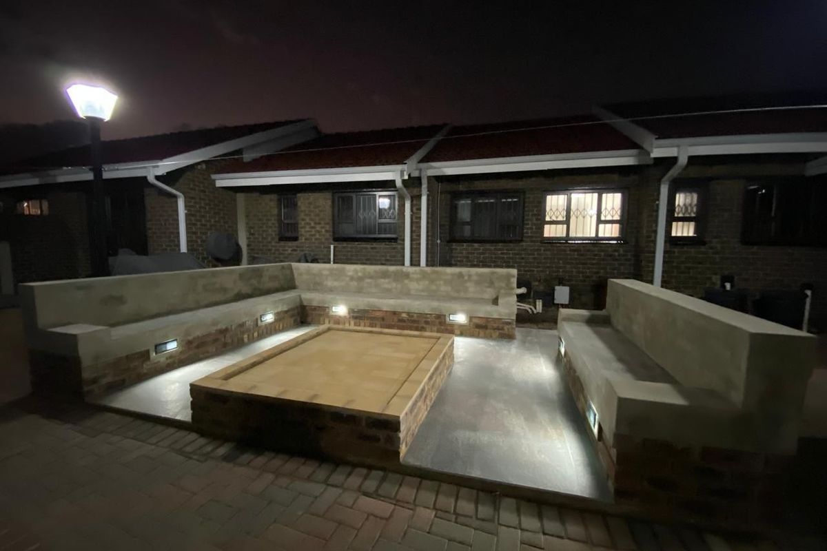 A well-lit rear patio area featuring built-in concrete seating and a central brick fire pit, perfect for outdoor entertaining.