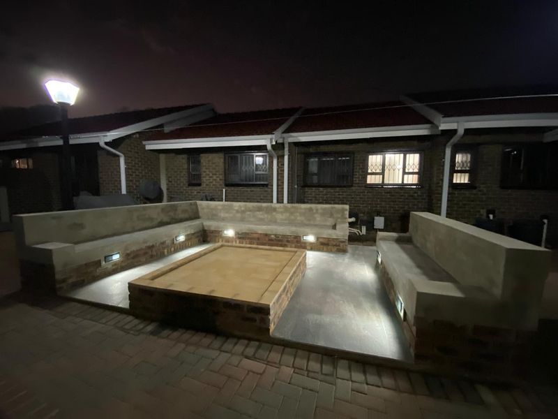 A well-lit rear patio area featuring built-in concrete seating and a central brick fire pit, perfect for outdoor entertaining.