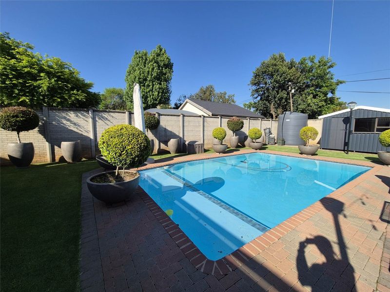 A well-maintained outdoor pool area featuring brick paving, a surrounding precast wall, a water storage tank, and a garden shed.