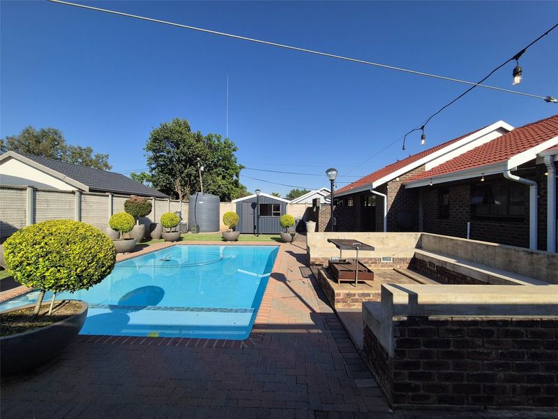 Outdoor entertainment area featuring a swimming pool, built-in braai, masonry seating, and paved patio space within a secure walled garden.