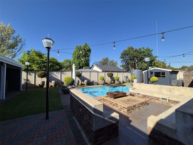 Outdoor entertainment area featuring a swimming pool, built-in brick seating, a central fire pit, and paved patio space within a secure perimeter.