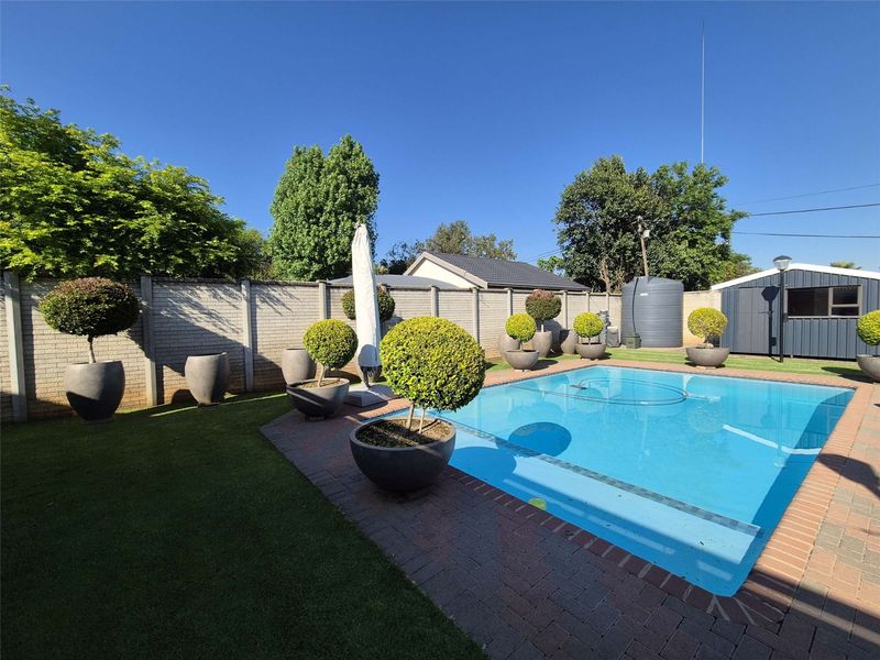 A well-maintained outdoor pool area featuring brick paving, a surrounding precast wall, a water storage tank, and a garden shed.