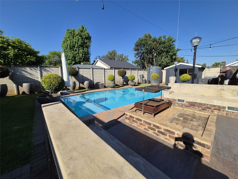 Outdoor entertainment area featuring a swimming pool, paved patio, and a built-in braai, enclosed by a secure brick boundary wall.