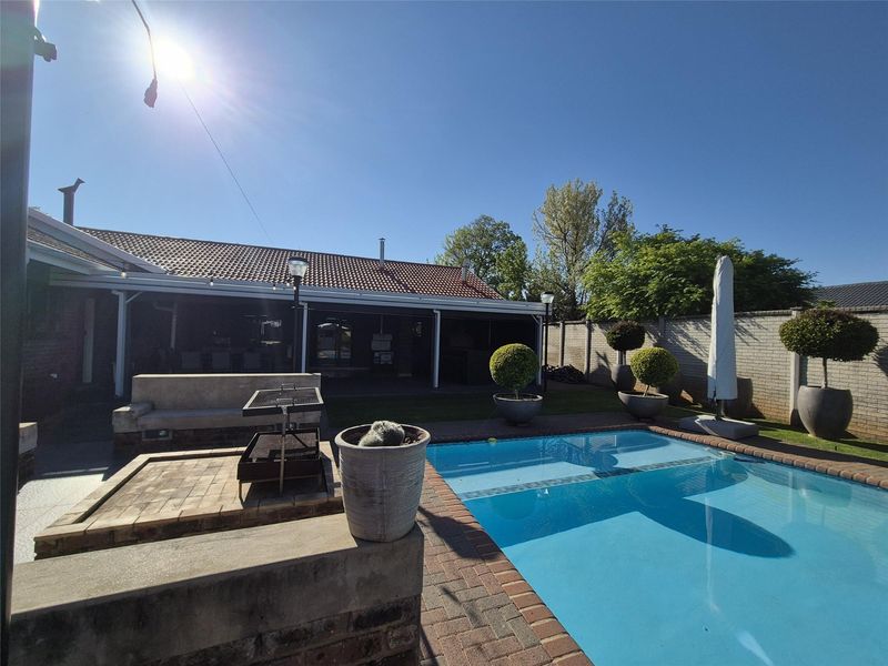 Outdoor entertainment area featuring a swimming pool, brick paving, and a built-in braai, adjacent to a covered patio and enclosed by a brick wall.
