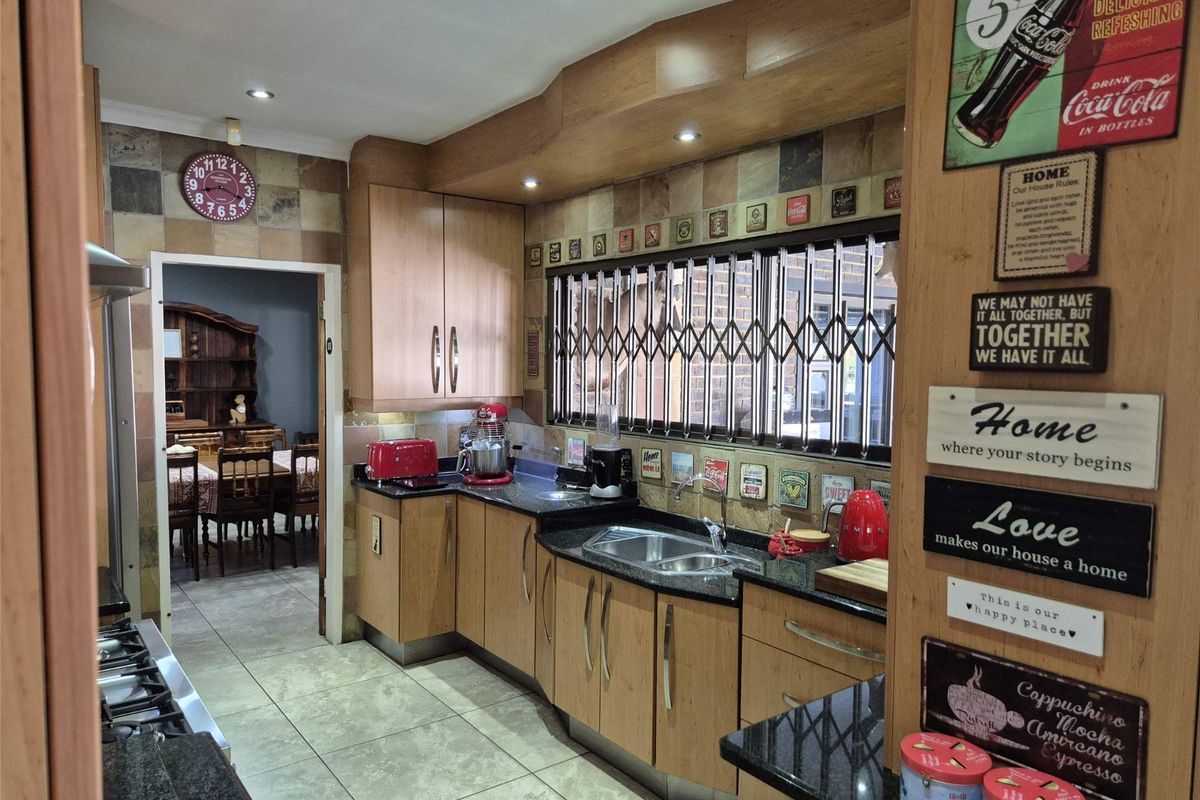 A functional kitchen featuring light wood cabinetry, dark granite countertops, a double sink, and a gas hob with an extractor fan.