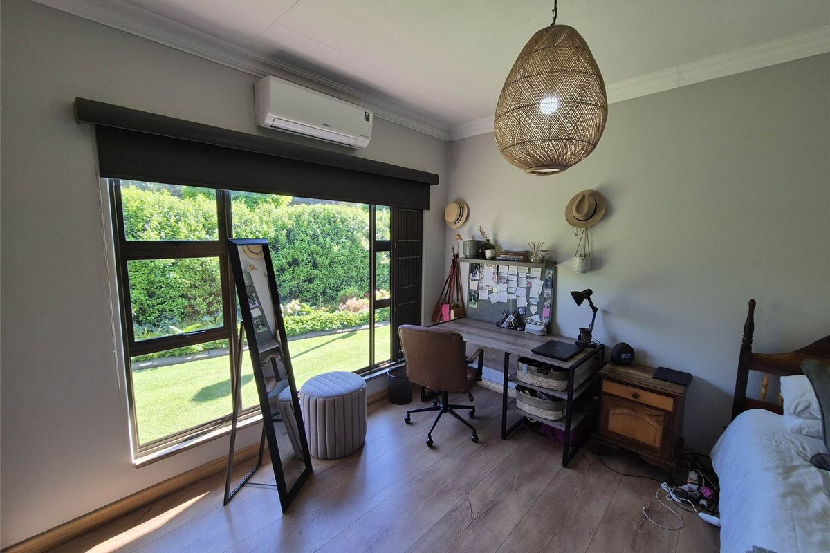 A well-maintained bedroom featuring laminate flooring, a split-system air conditioner, and large windows overlooking the garden.