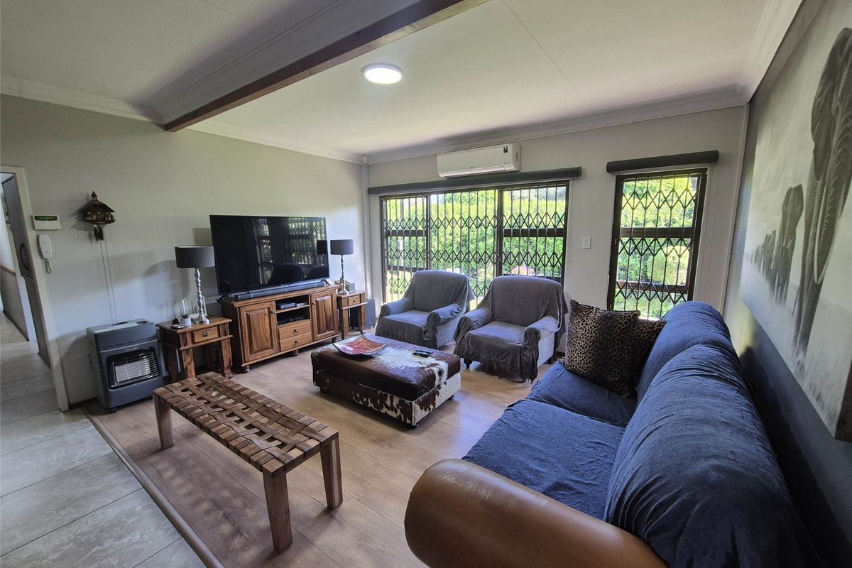 A comfortable living room featuring laminate flooring, a split-system air conditioner, and large sliding glass doors with security gates for natural light.