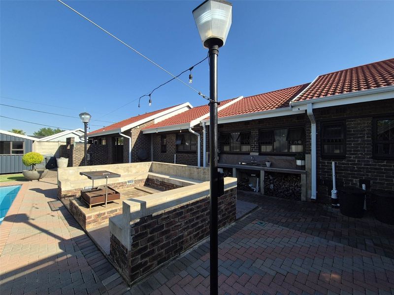 Outdoor entertainment area featuring a paved patio, built-in brick braai, integrated seating, and an outdoor sink, adjacent to a swimming pool.