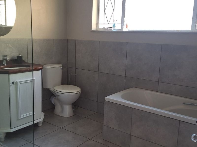A functional bathroom featuring tiled walls and flooring, a built-in bathtub, a vanity cabinet with a basin, and a toilet.