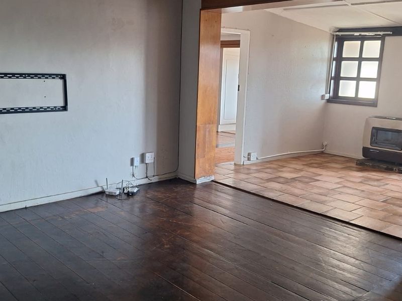 An open-plan living area featuring dark timber flooring, a secondary tiled space with a wood-burning stove, and a wall-mounted television bracket.