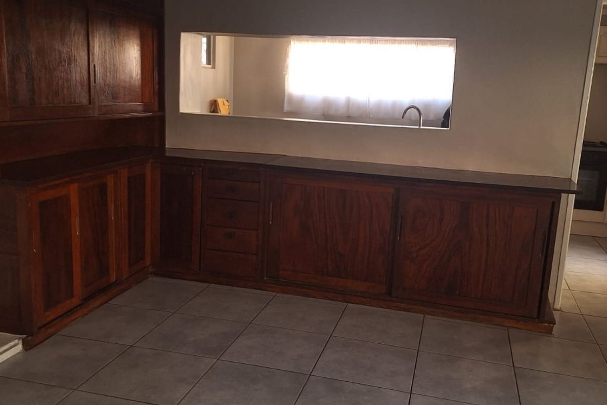A functional kitchen area featuring extensive built-in wooden cabinetry, tiled flooring, and a convenient pass-through window connecting to the adjacent space.
